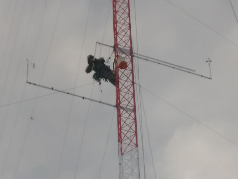 Technician working at height on a guyed tower in heavy overcast