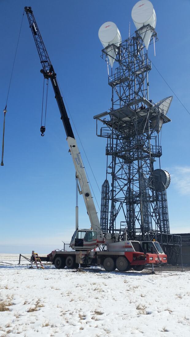 Hydraulic crane set up on a snow-covered tower site under clear sky