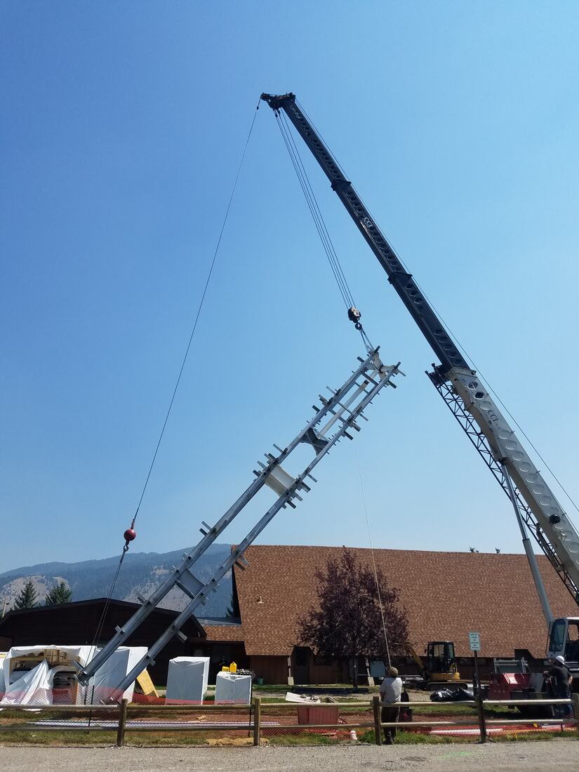Crane lifting a galvanized lattice section into place beside a building