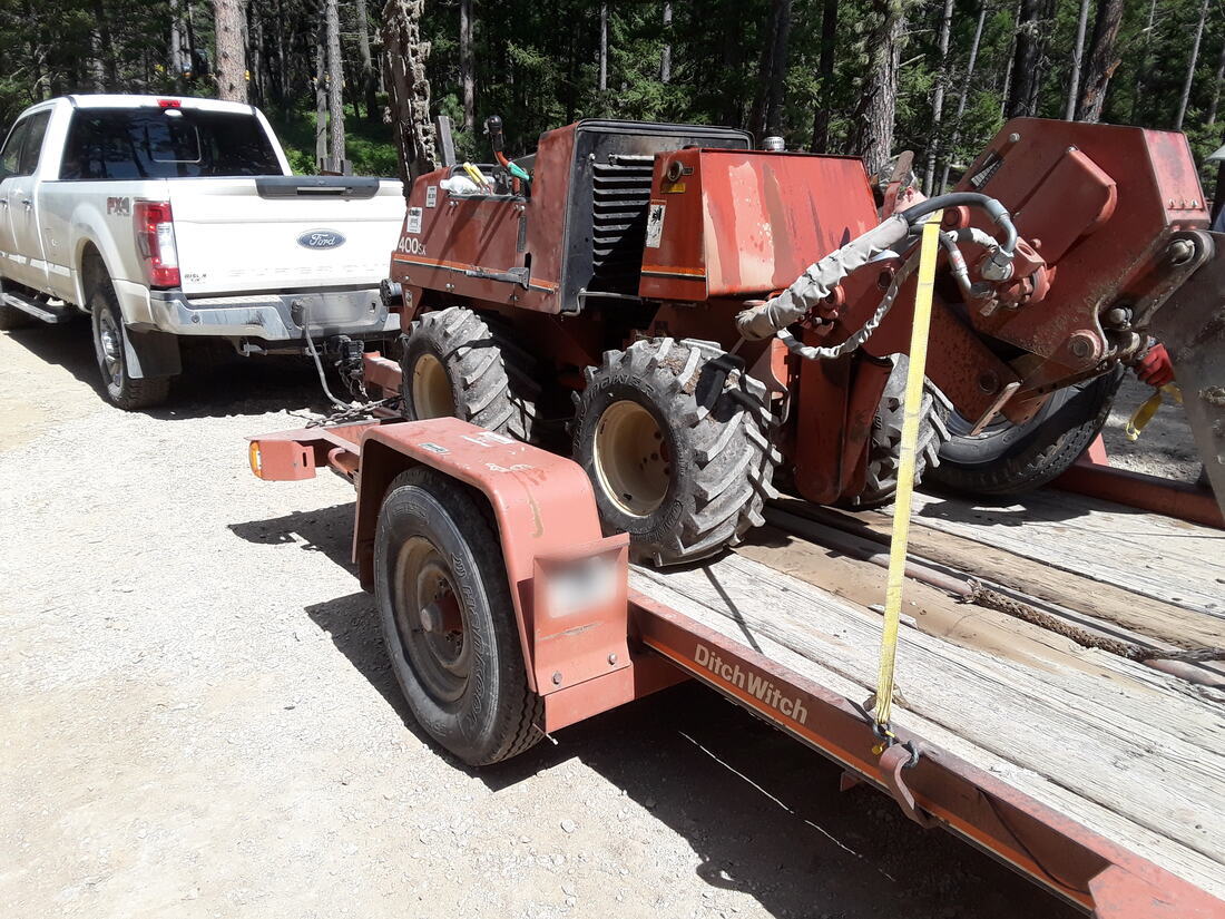 Ditch Witch trencher loaded on a trailer behind a crew truck on a forest access road