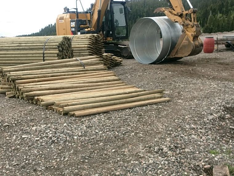 Excavator, culvert and pole stock staged for access road construction