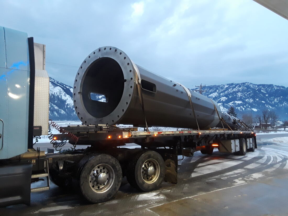 Steel monopole section chained down on a flatbed with snowy mountains behind