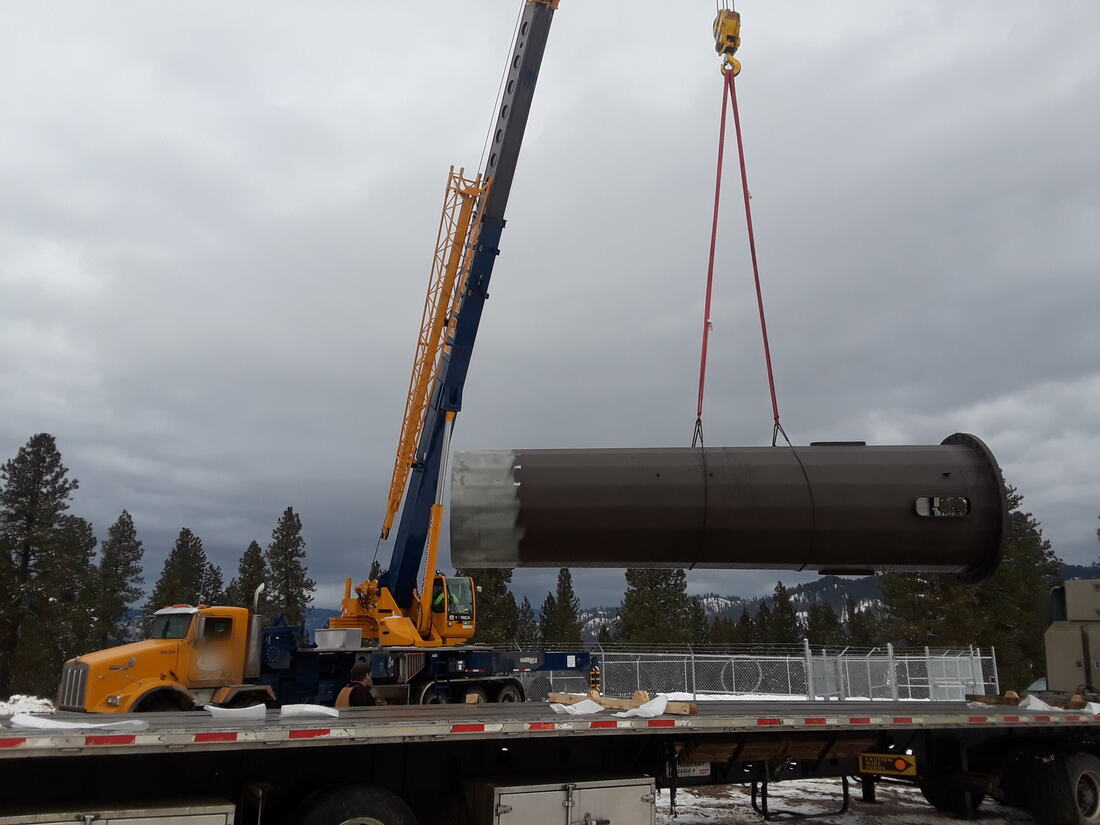 Hydraulic crane lifting a monopole section clear of a flatbed trailer
