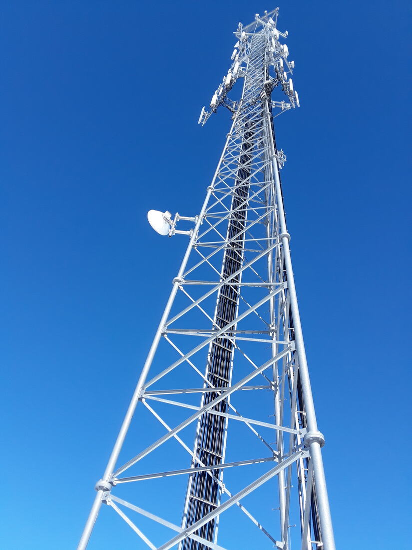 Galvanized self-support tower against a deep blue sky, viewed from the base