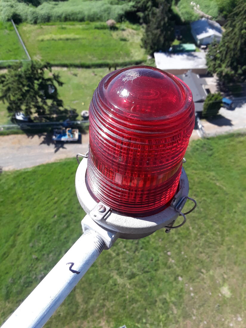 Red obstruction beacon at the top of a tower with fields far below
