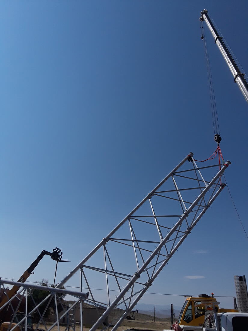 Crane lifting a galvanized lattice tower section against blue sky