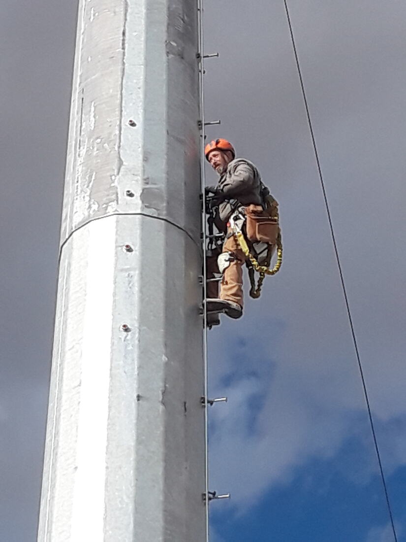 Tower technician in full harness climbing a galvanized monopole
