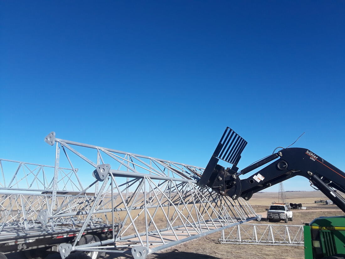 Telehandler unloading galvanized tower sections from a trailer on the prairie