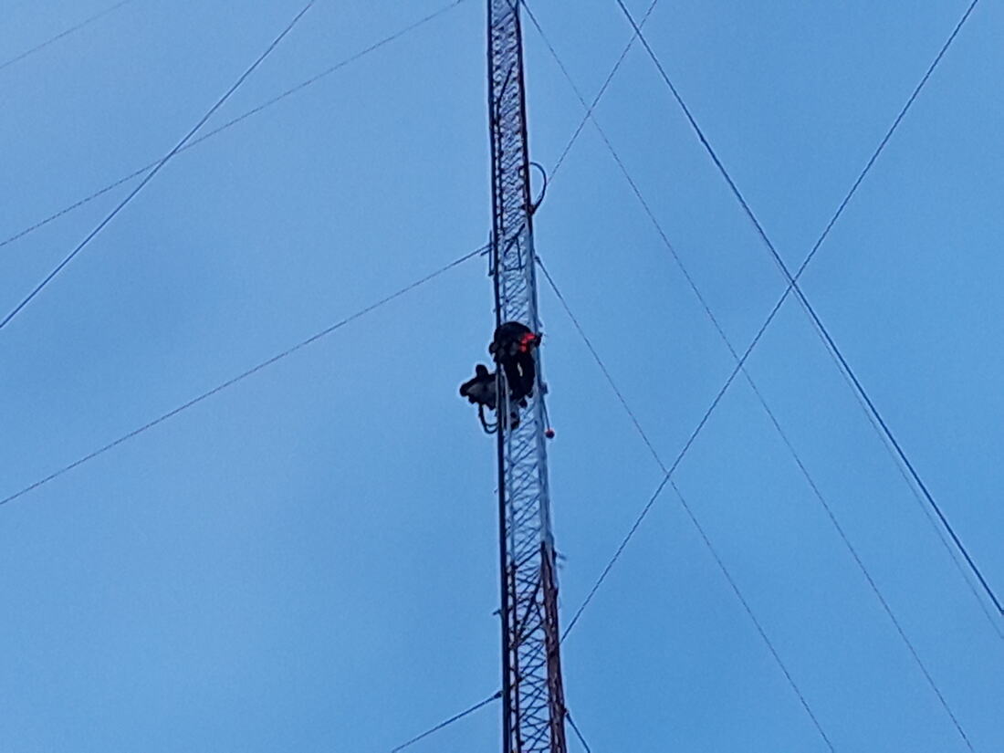 Technician climbing a guyed tower against a clear sky