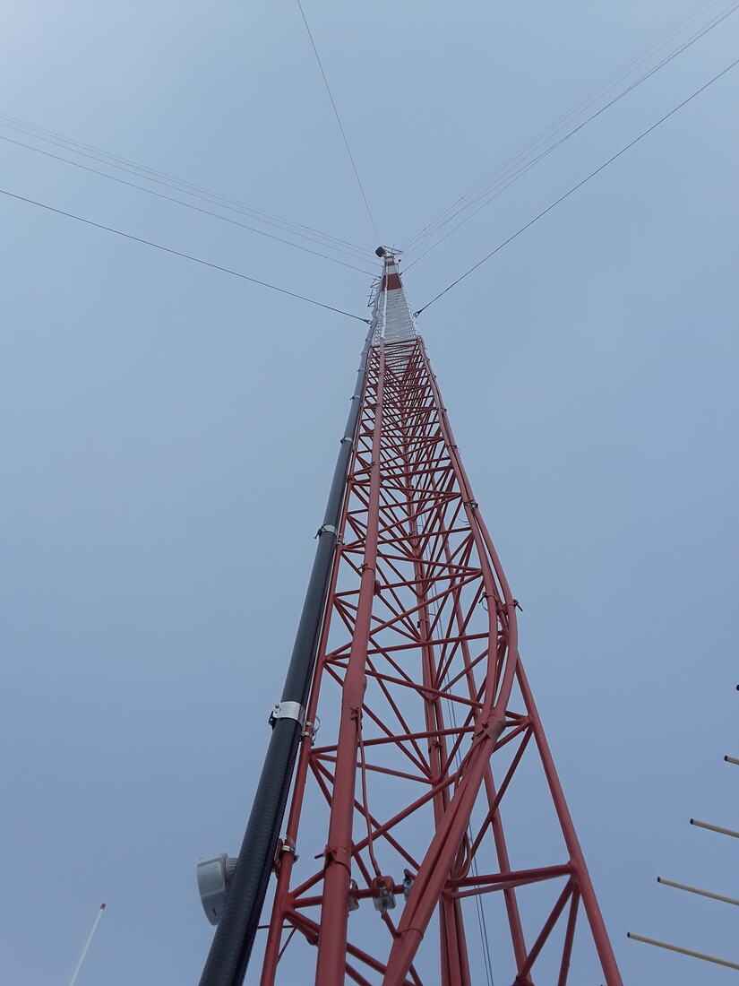 Red and white guyed tower with a gin pole rigged at the top