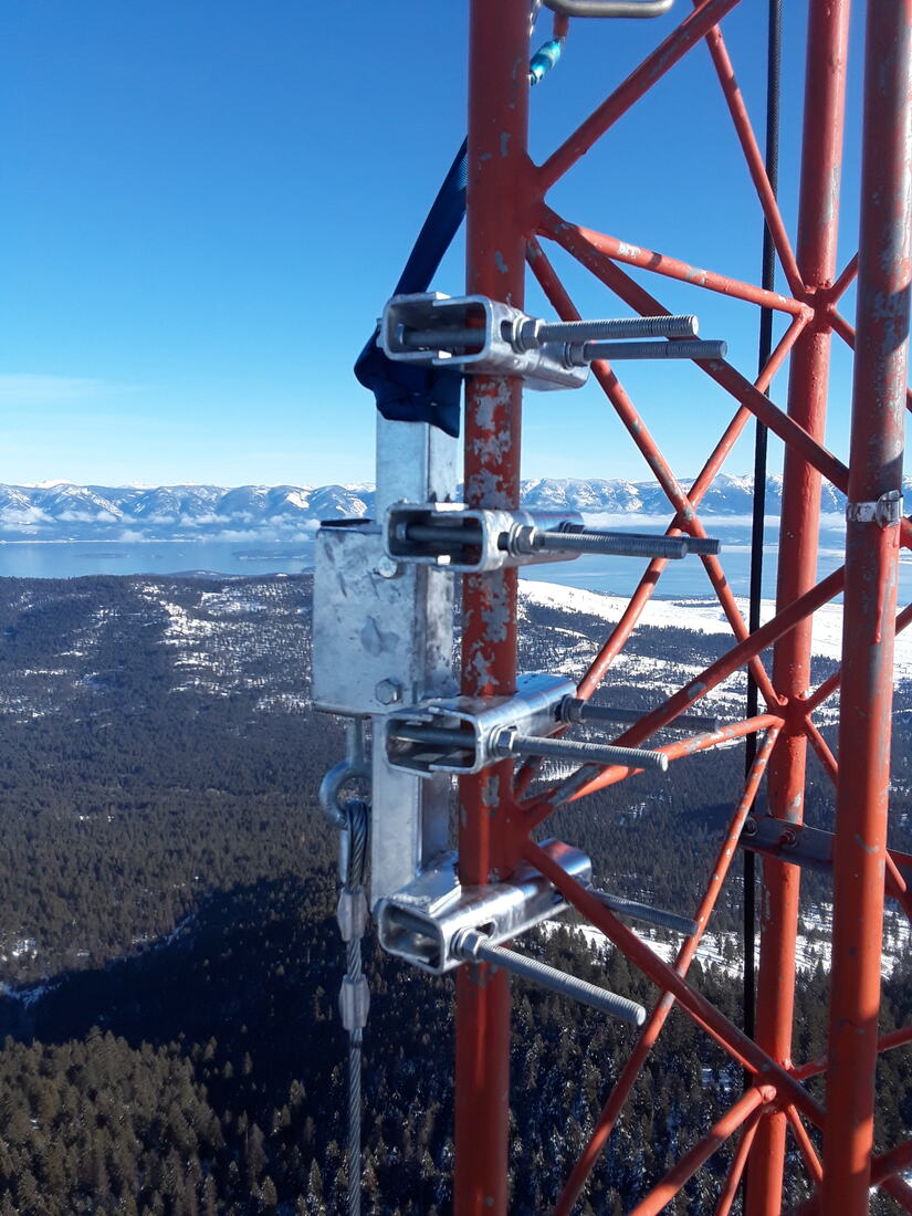 Antenna mounts on a red tower with a lake and mountains far below