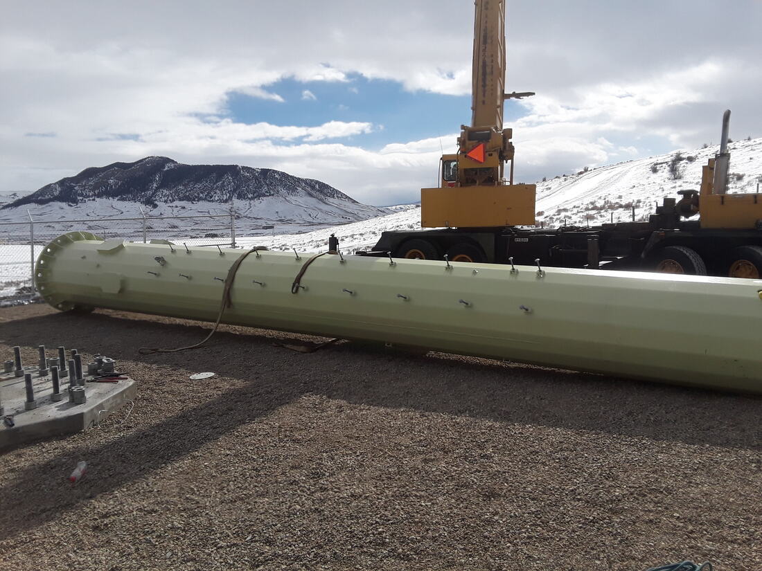 Monopole section on the ground beside a crane on a snowy site