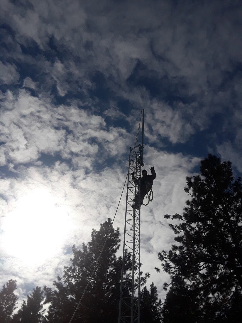 Silhouette of a climber on a lattice tower against sun and clouds