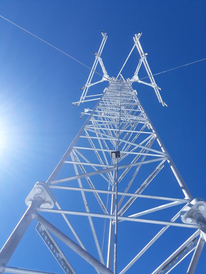 Guyed lattice tower and guy wires against blue sky with sun flare