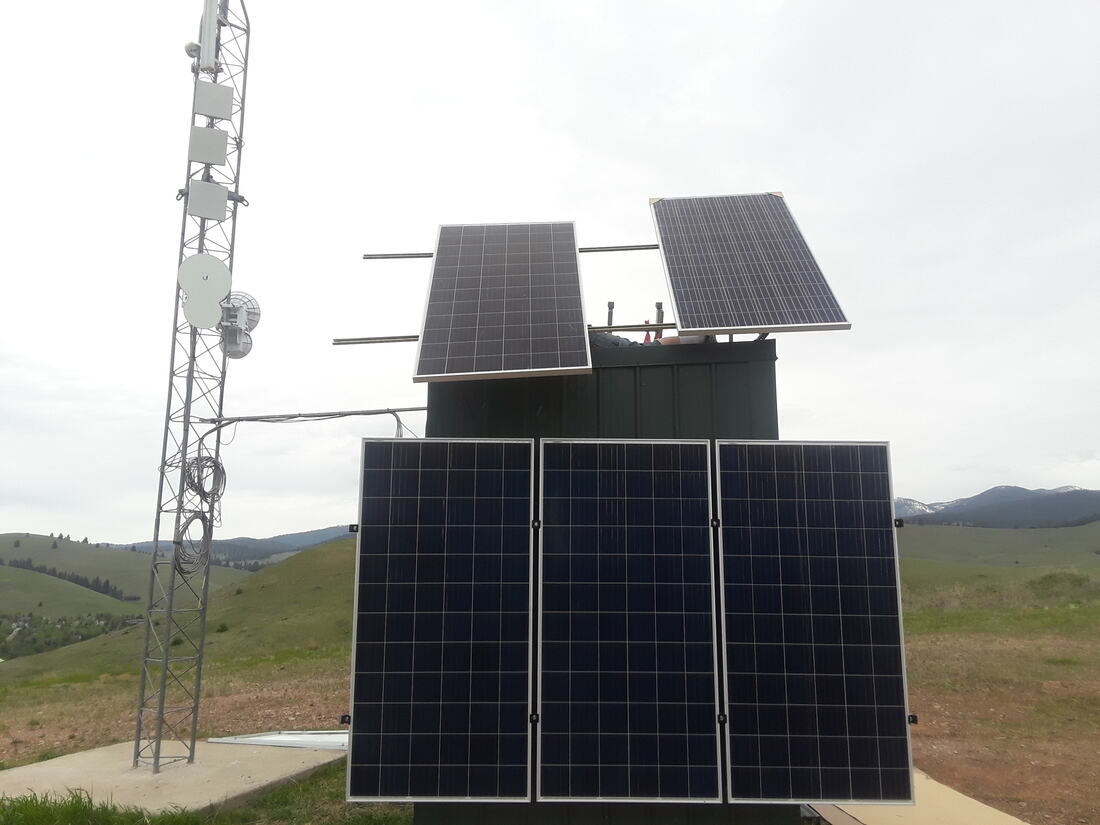 Solar array and equipment shelter beside a lattice tower on open range