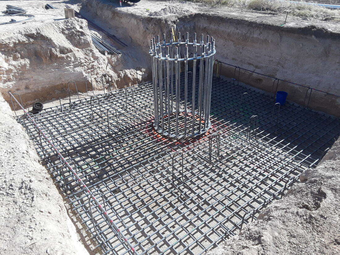 Anchor bolt cage standing on a tied rebar mat in a foundation excavation