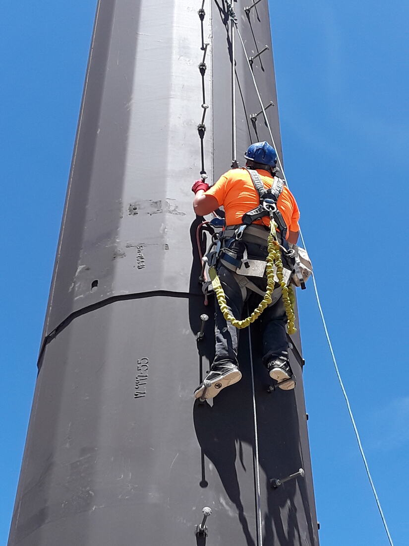 Technician in high-visibility gear working on a monopole flange